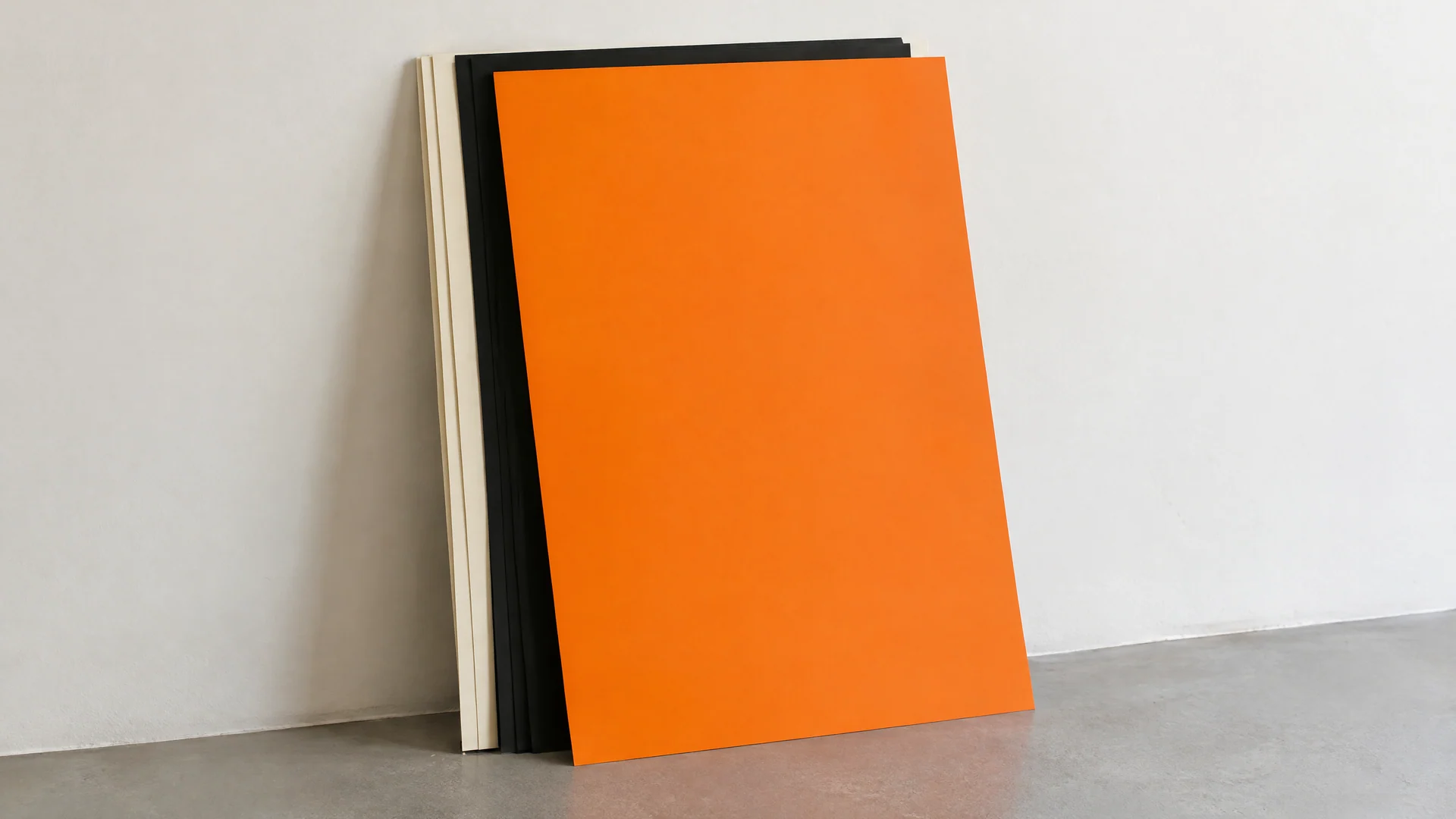 Stack of blank orange, black and cream poster sheets leaning on a wall