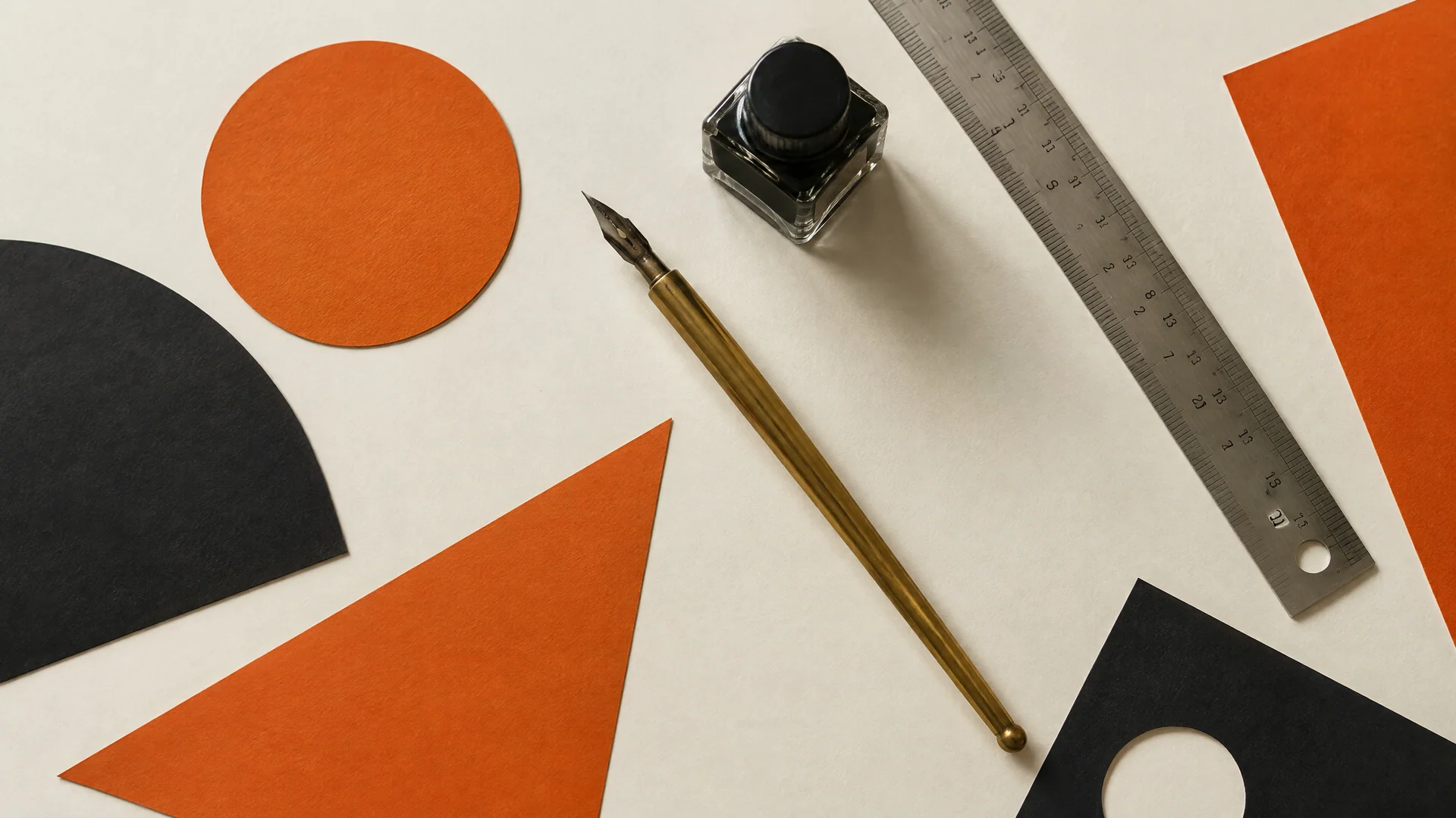 Brass pen, ink bottle, steel ruler and cut-paper shapes on cream paper